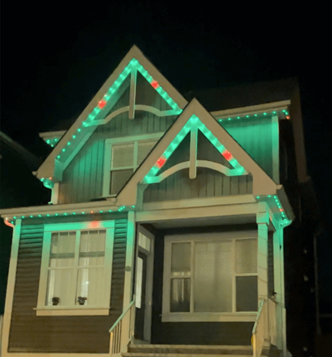 Permanent roofline lighting switched to green holiday colors on a gabled home at night