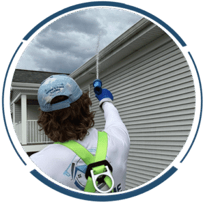 Near Me Exteriors crew member on a ladder working along the gutter line of a vinyl-sided house