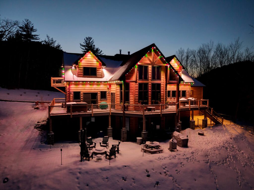 Warm exterior lights outlining the roofline of a snow-covered home at dusk